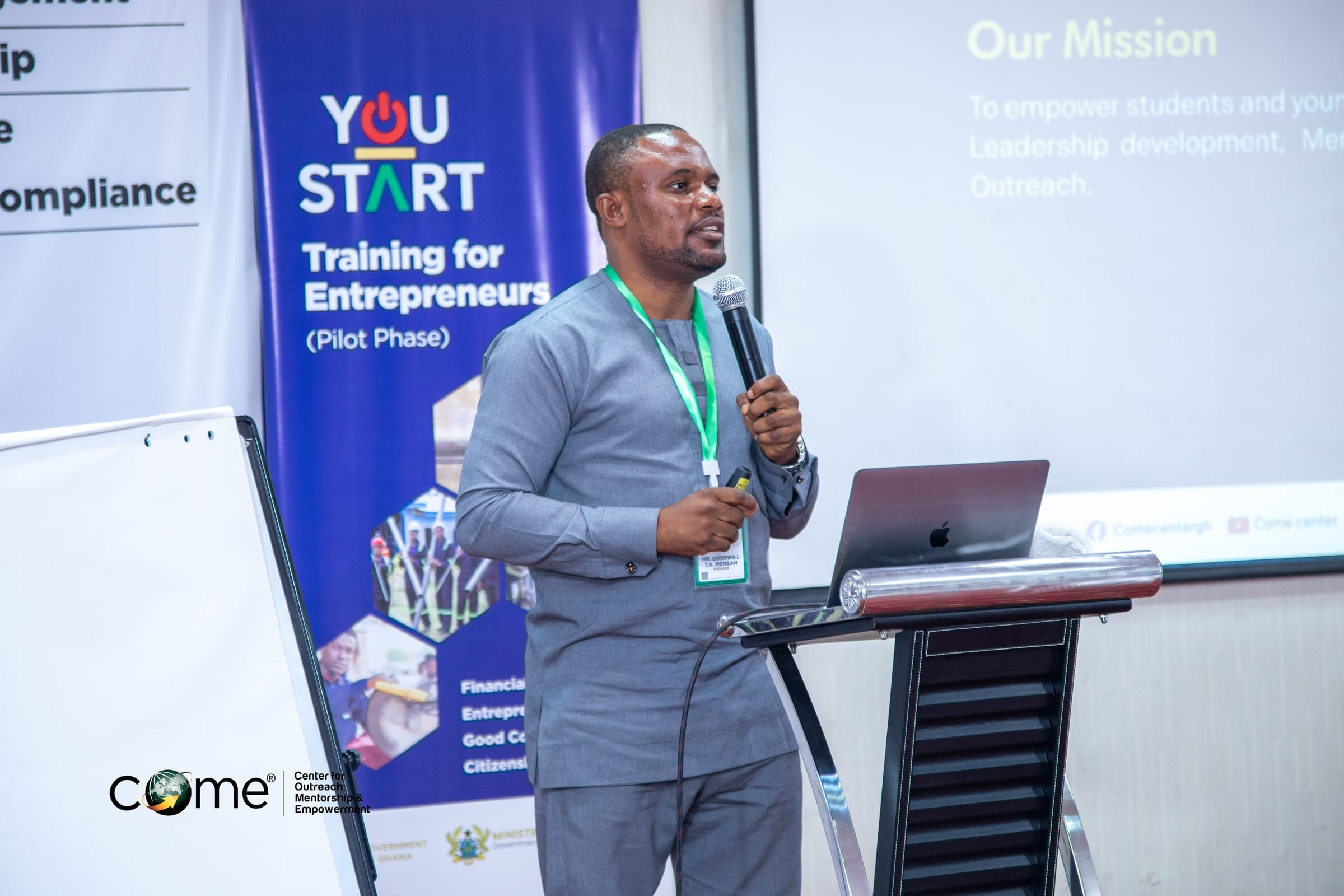Bright campus-style building with reflective glass, trees, and red flowers in the foreground.