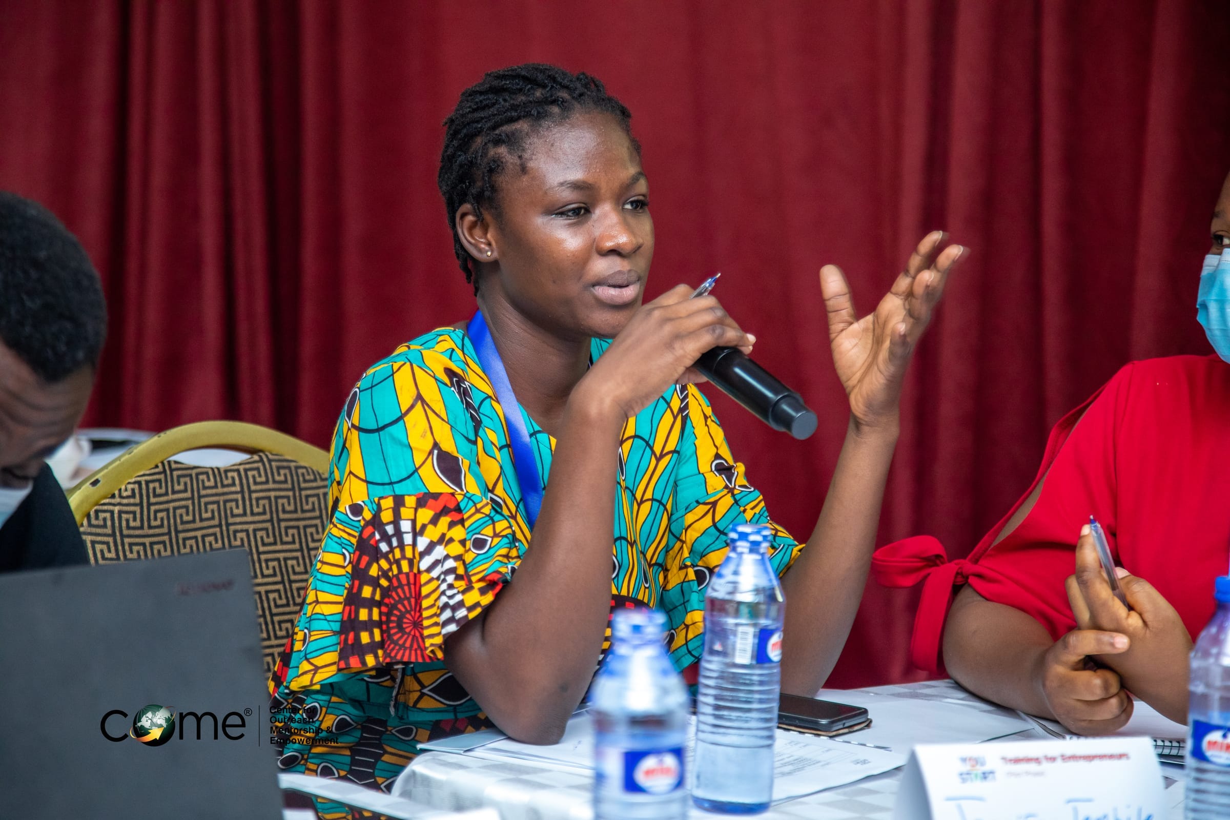 Participant speaking into a microphone at a COME training and entrepreneurship session.
